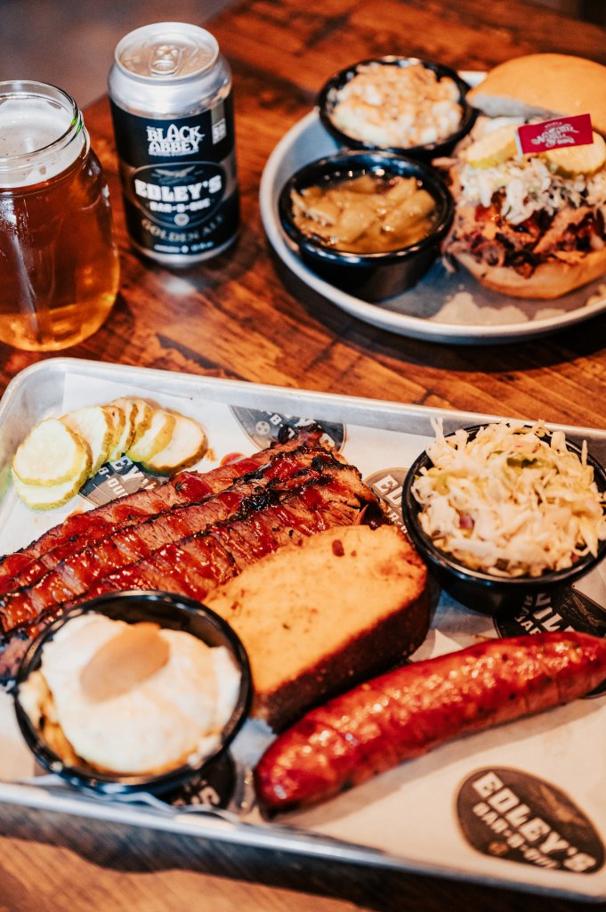 Top 10 Barbecue Joints in Franklin That Will Keep You Coming Back for Seconds A hearty barbecue platter featuring smoked ribs, sausage, baked beans, coleslaw, and cornbread, accompanied by a can of Golden Ale and a glass of beer in Williamson County, Tennessee.
