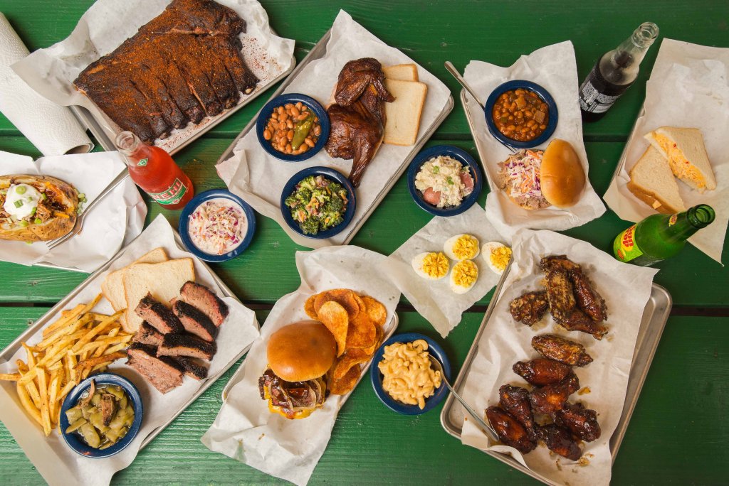 A variety of barbecue dishes including ribs, chicken, brisket, and sides like beans, coleslaw, and mac and cheese, all served on a green picnic table in Williamson County, Tennessee.