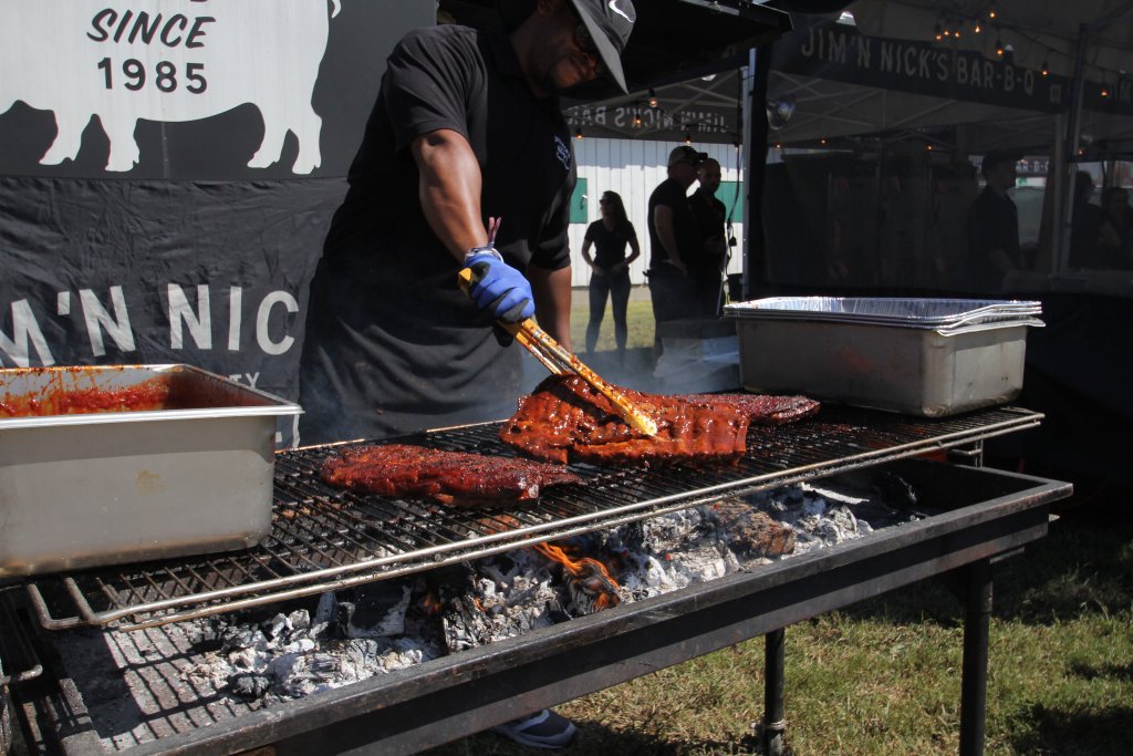 A skilled chef grills ribs at an outdoor barbecue event, using tongs to turn the meat over a roaring fire in Williamson County, Tennessee.