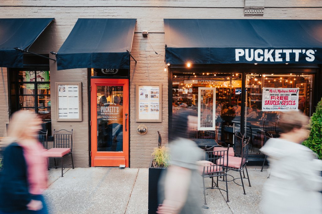 A bustling restaurant scene with patrons dining outside under black awnings at Puckett's in Williamson County, Tennessee.