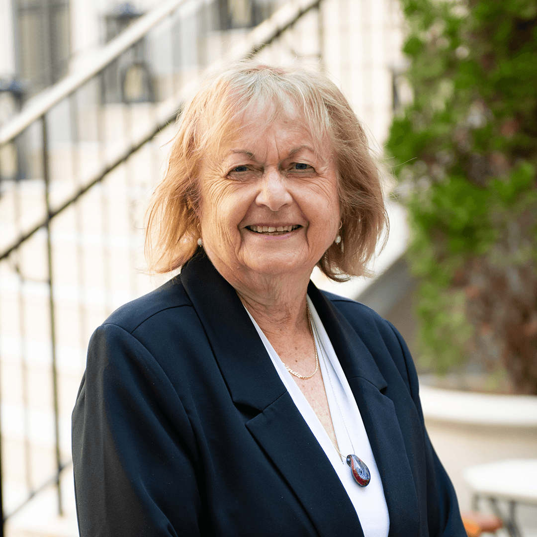 A smiling woman with short blonde hair wearing a black blazer and a white blouse stands in front of a staircase with greenery in the background in Williamson County, Tennessee.