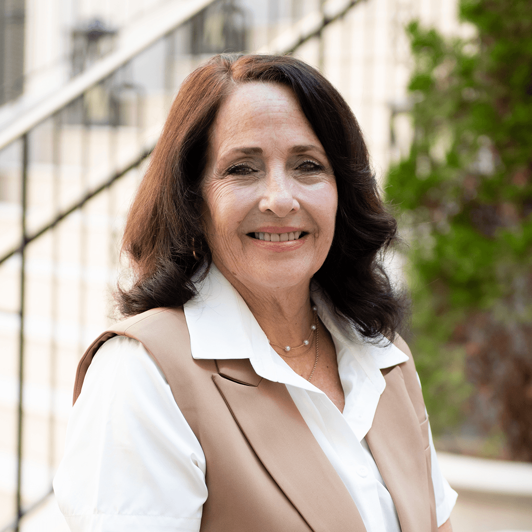 A woman with shoulder-length dark hair is smiling warmly at the camera, wearing a beige vest over a white blouse in Williamson County, Tennessee.