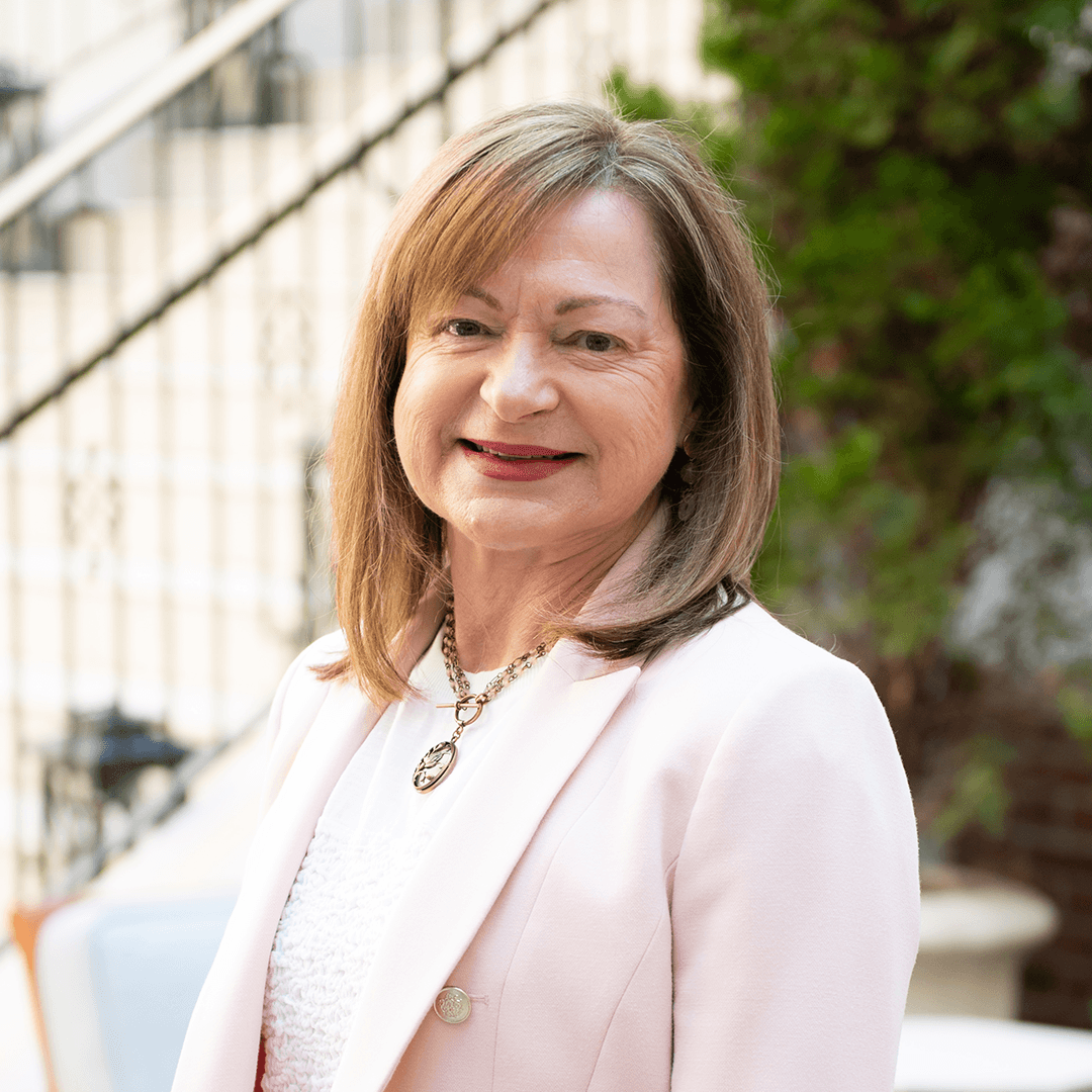 A woman with shoulder-length brown hair is smiling warmly, wearing a light pink blazer over a white top, with a delicate necklace featuring a pendant in Williamson County, Tennessee.