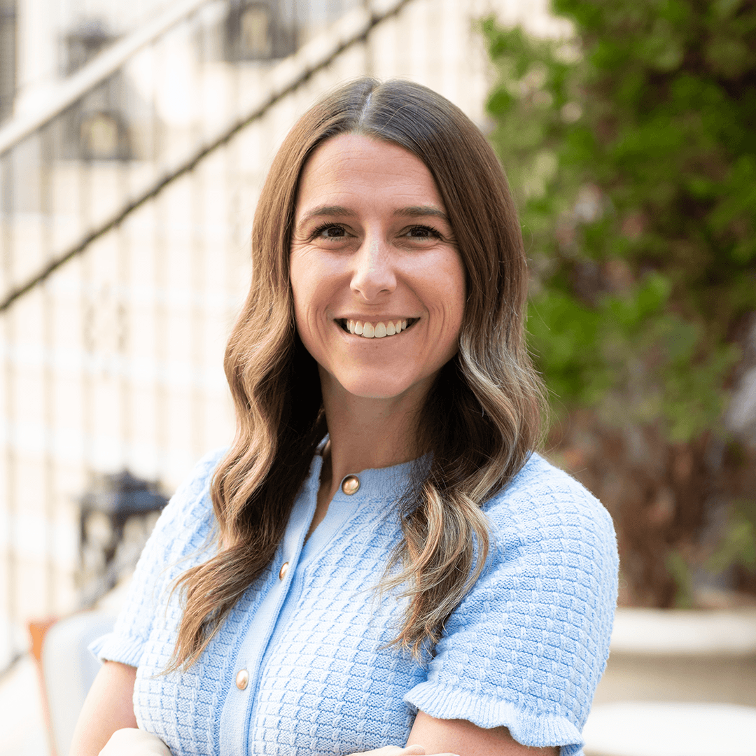 A woman with long, wavy brown hair is smiling warmly at the camera, wearing a light blue, textured button-up sweater in Williamson County, Tennessee.