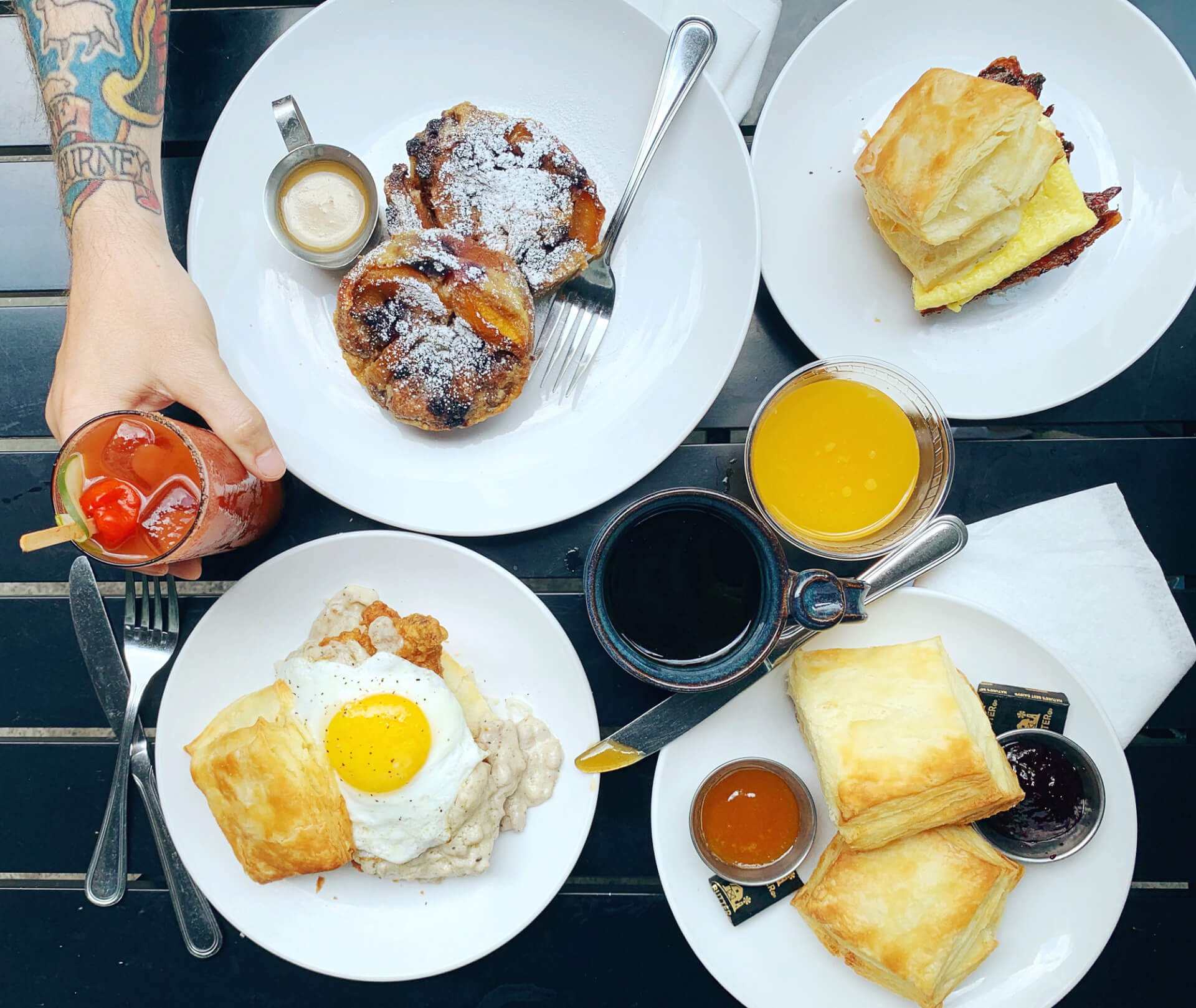 A variety of breakfast items including pastries, biscuits, eggs, and drinks are spread across several white plates on a black table in Williamson County, Tennessee.