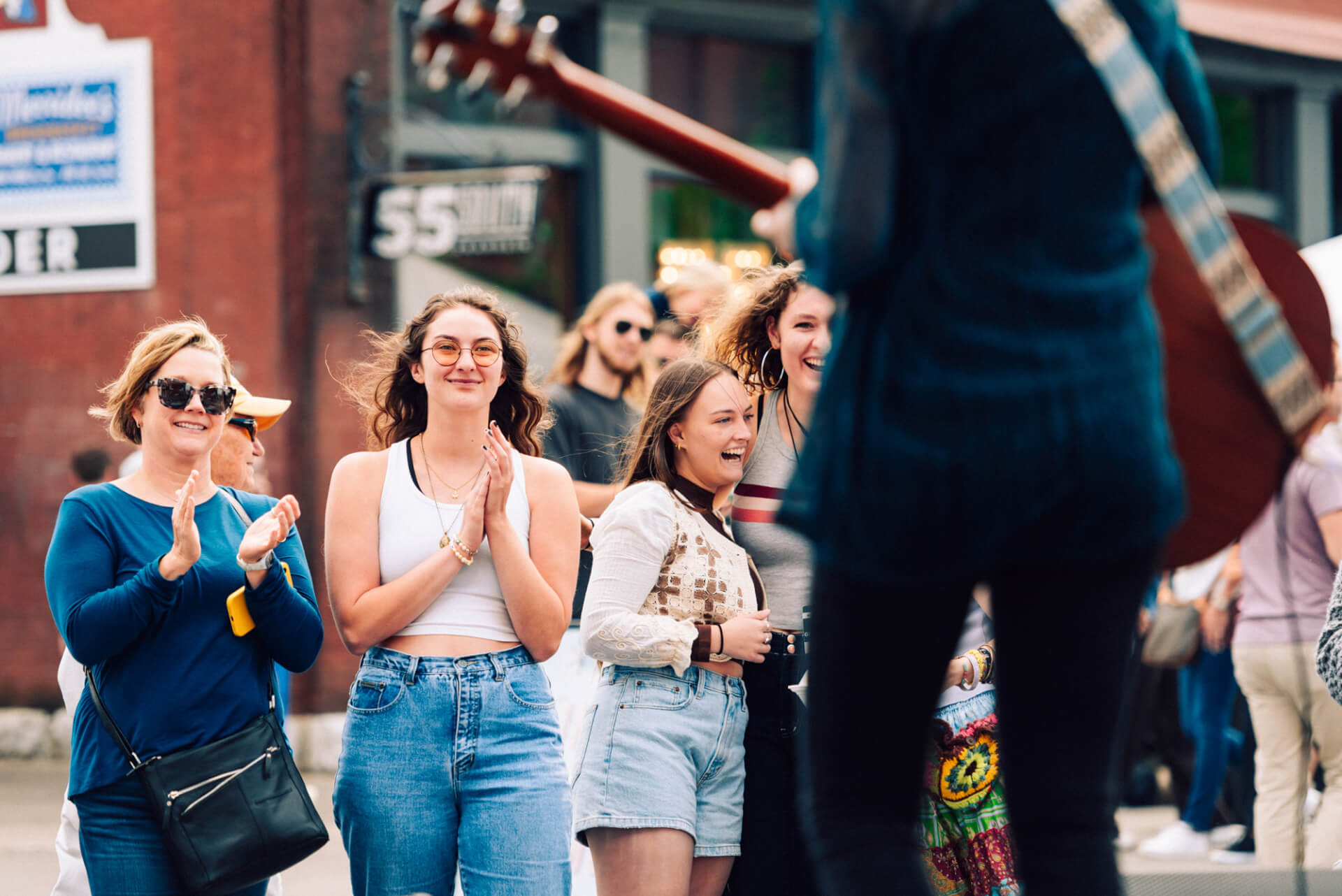 A lively crowd of young women clapping and laughing while a musician plays guitar in the street in Williamson County, Tennessee.
