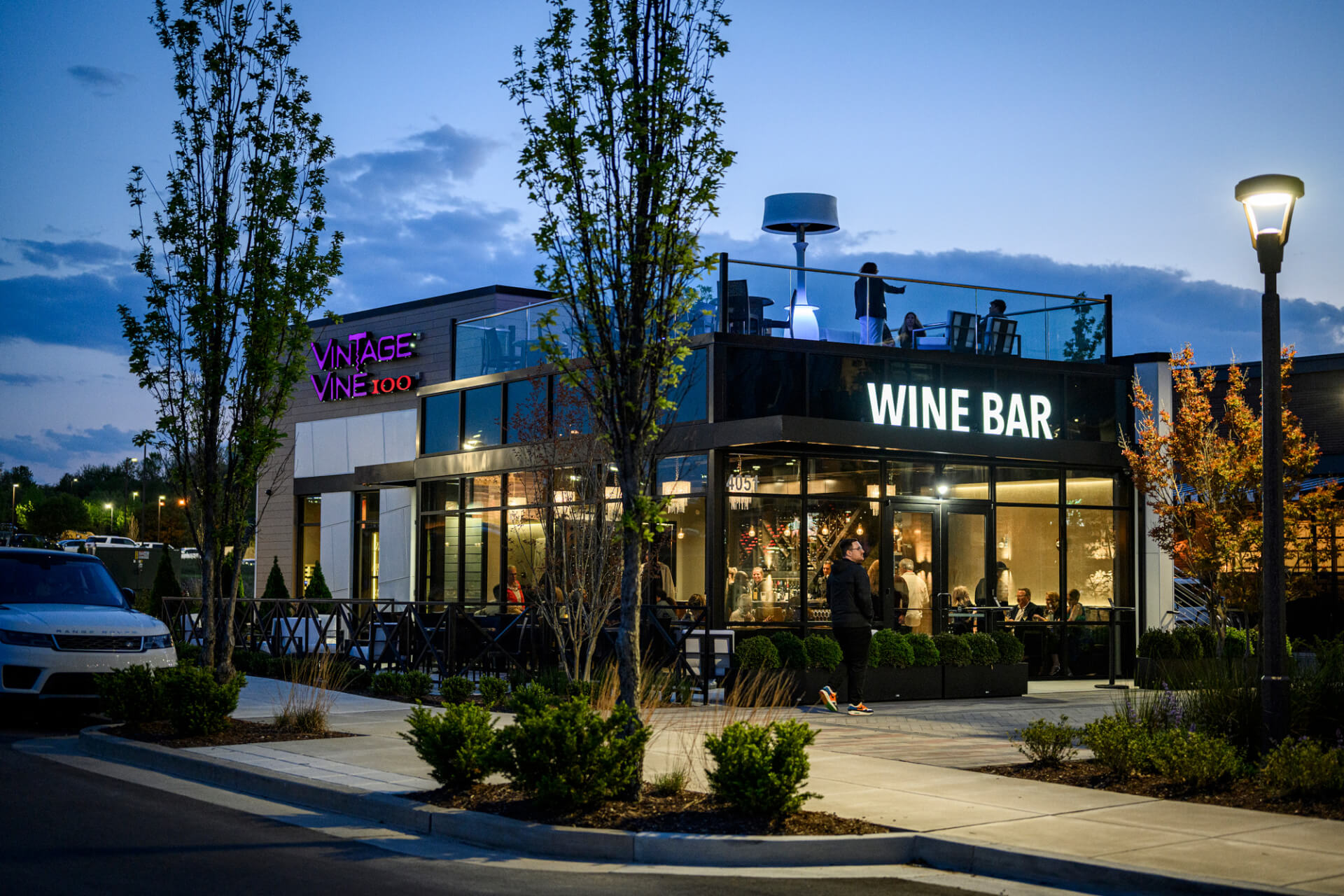 A modern wine bar with a rooftop patio, illuminated by neon signs and outdoor lighting, as dusk falls in Williamson County, Tennessee.