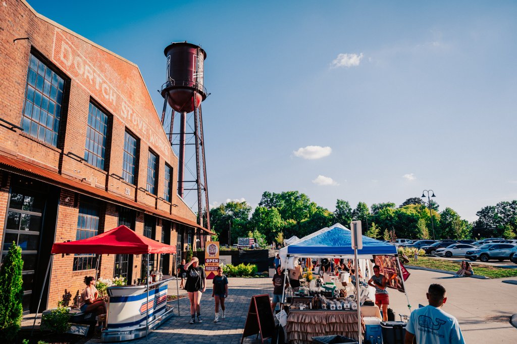 A bustling outdoor market with colorful tents and vendors set up in front of a historic brick building and a vintage water tower in Williamson County, Tennessee.