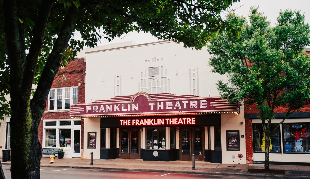 End of Summer Escape The Franklin Theatre, a historic movie theater with a vibrant marquee, stands prominently on a tree-lined street in a quaint town in Williamson County, Tennessee.