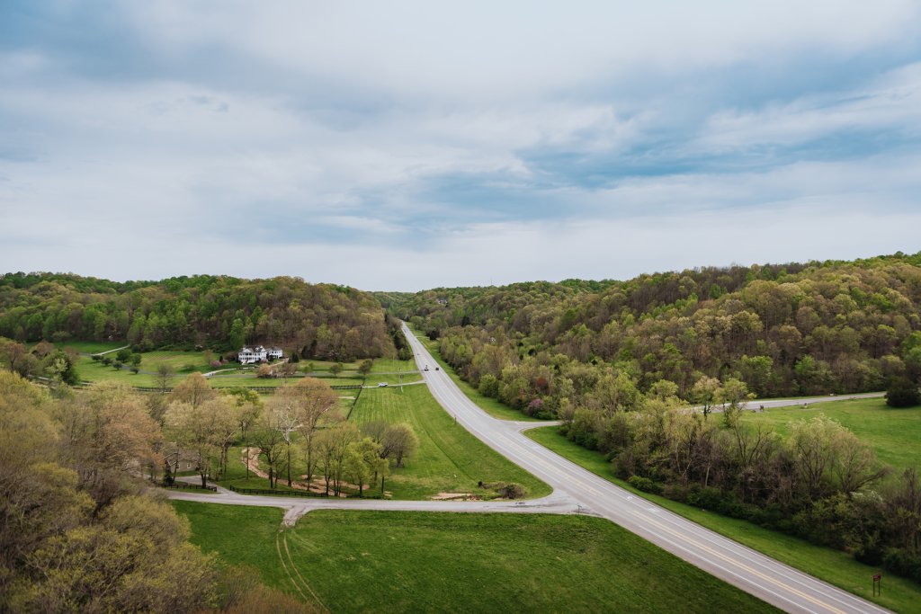 End of Summer Escape A scenic view of a winding road through lush green hills and forests, with a distant house nestled among the trees in Williamson County, Tennessee.