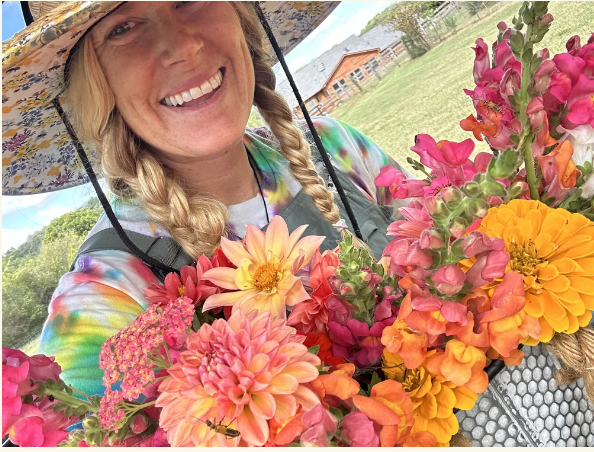 U-Pick Flowers A woman with braided hair and a floral hat smiles brightly while holding a vibrant bouquet of colorful flowers in Williamson County, Tennessee.