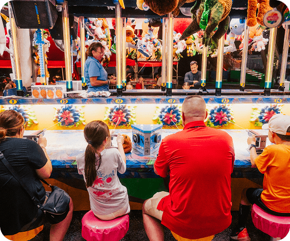 A family enjoys a lively game of Whack-a-Mole at an arcade, surrounded by colorful lights and toys in Williamson County, Tennessee.