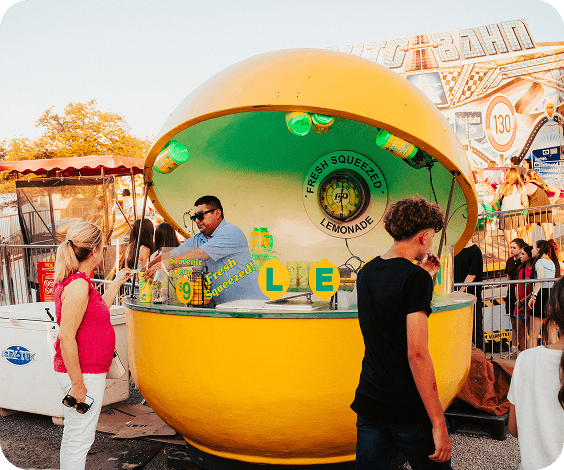 A vibrant yellow lemonade stand shaped like a giant lemon at a bustling fairground in Williamson County, Tennessee.