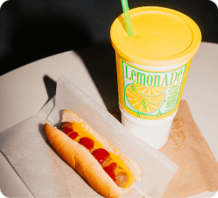 A hot dog with mustard on a bun next to a yellow lemonade cup with a straw in Williamson County, Tennessee.