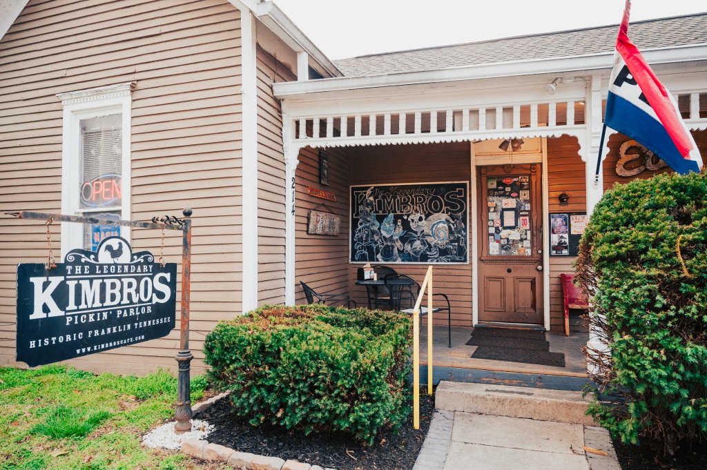The 8 Best Late-Night Spots for Live Music, Cocktails & More in Franklin A quaint, historic building with a welcoming porch, featuring a sign for 'The Legendary Kimbros Pickin' Parlor' and a vibrant chalkboard menu in Williamson County, Tennessee.