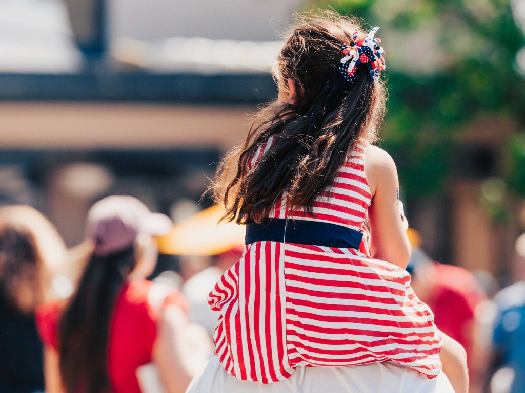 A young girl in a red, white, and blue striped dress sits on someone's shoulders at a crowded outdoor event in Williamson County, Tennessee.