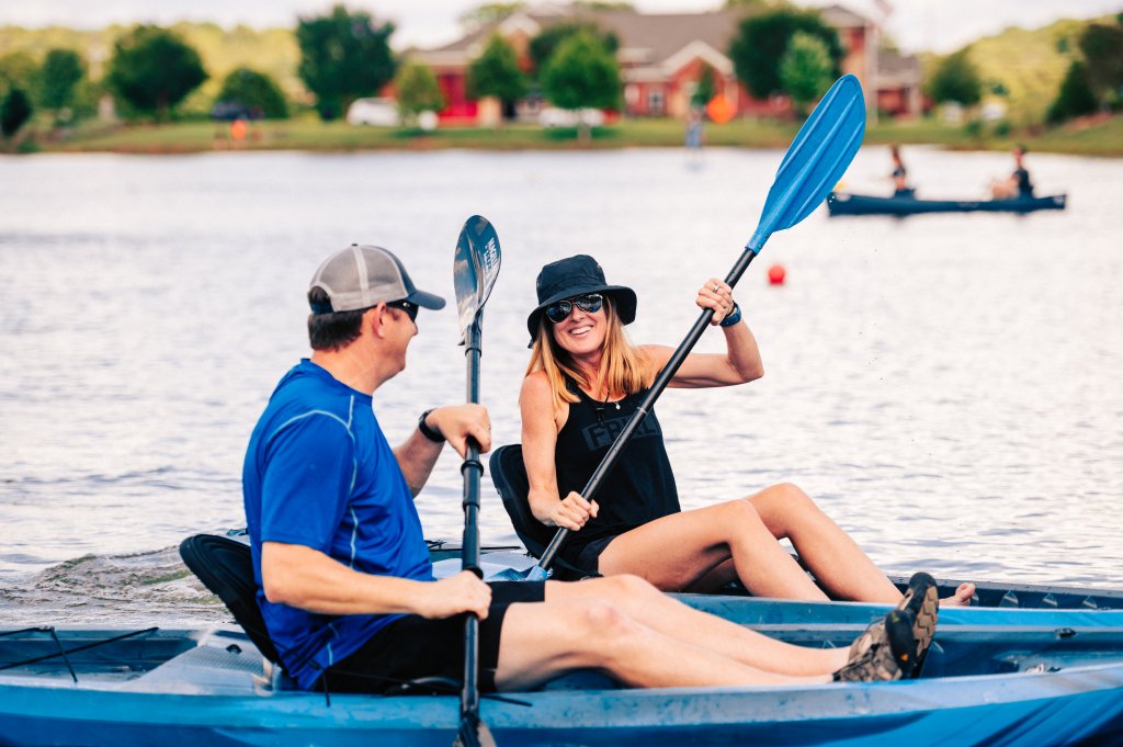 Your Best Summer Break Ever: Top Kid-Friendly Activities in Franklin, Tennessee A couple enjoys a leisurely kayak ride on a calm lake, surrounded by lush greenery and distant houses in Williamson County, Tennessee.