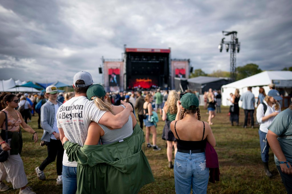 Things To Do A couple wearing matching green jackets and hats embrace at an outdoor music festival, with a large crowd and stage in the background in Williamson County, Tennessee.