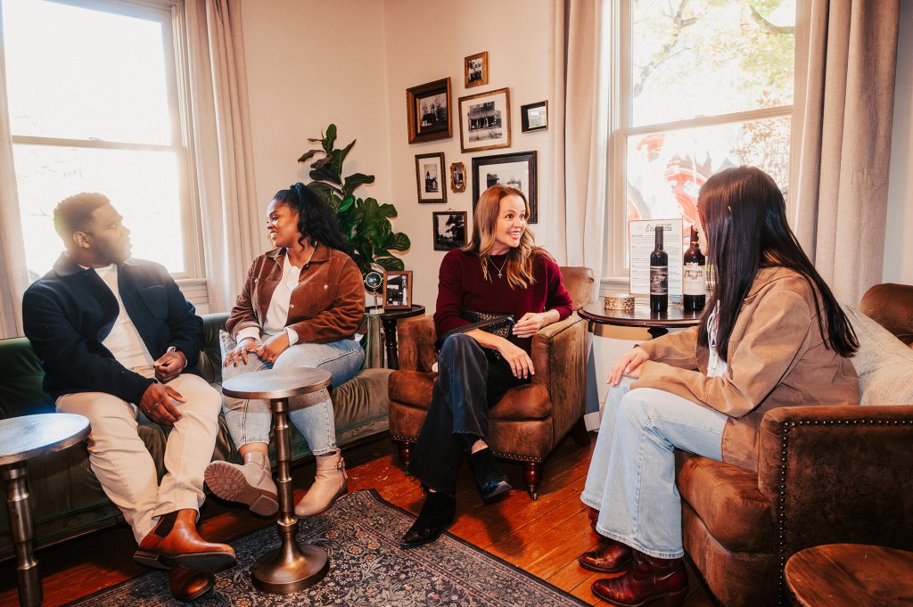 Things To Do Four friends enjoying a casual gathering in a cozy living room, sipping wine and engaging in conversation in Williamson County, Tennessee.