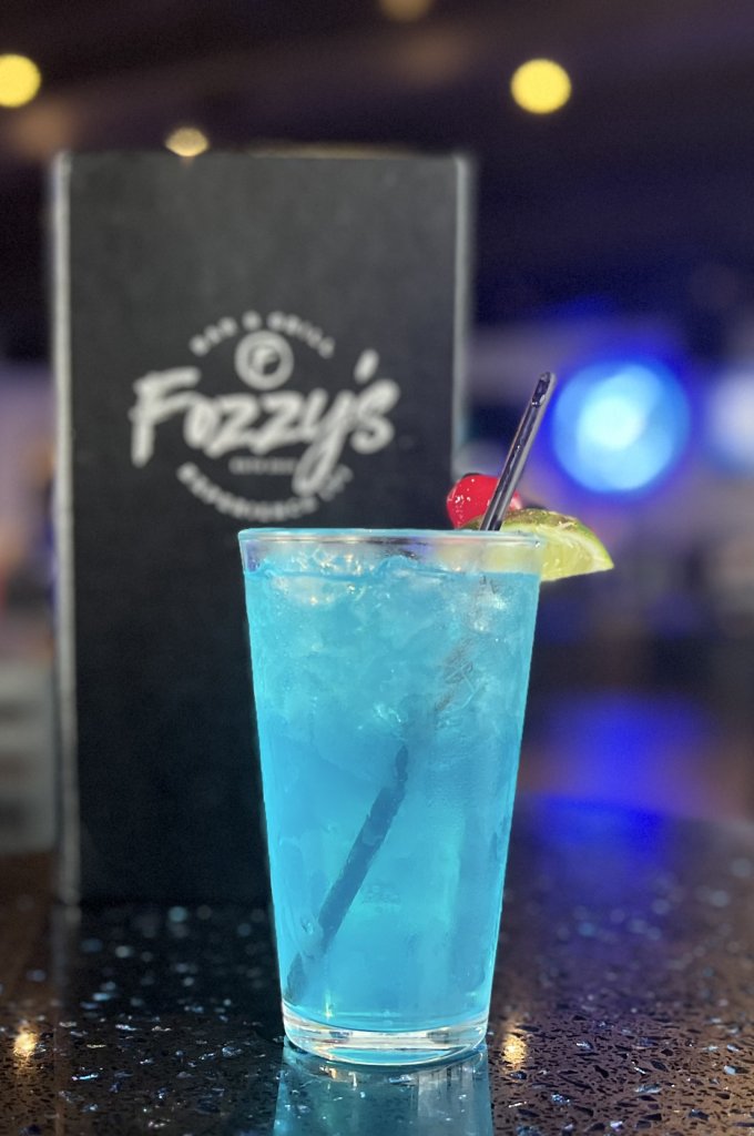 Fozzy's Bar & Grill - Franklin A vibrant blue cocktail garnished with a cherry and lime wedge, served in a tall glass with ice and a straw in Williamson County, Tennessee.