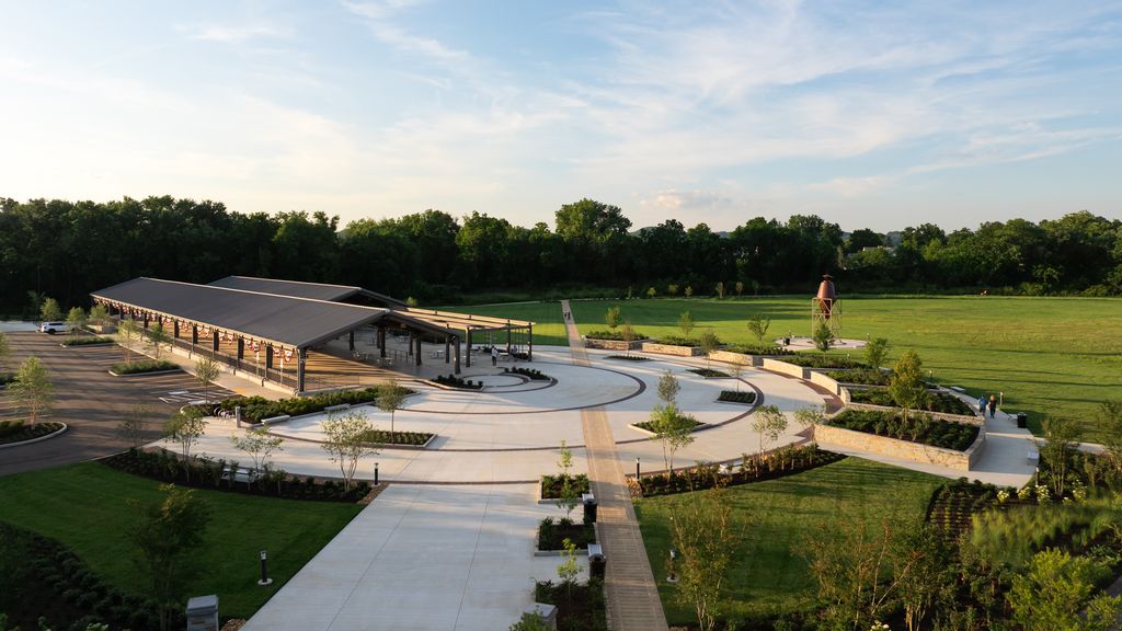 A modern pavilion with a curved roof and open sides sits in a lush park surrounded by trees and green fields in Williamson County, Tennessee.