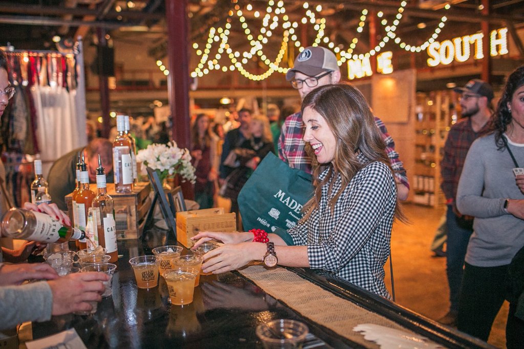 2026 MADE SOUTH Holiday Market A woman smiling while reaching for a drink at a crowded indoor event in Williamson County, Tennessee.