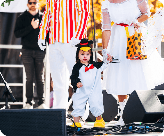 PumpkinFest A toddler in a penguin costume walks between two adults in costumes on a stage in Williamson County, Tennessee.