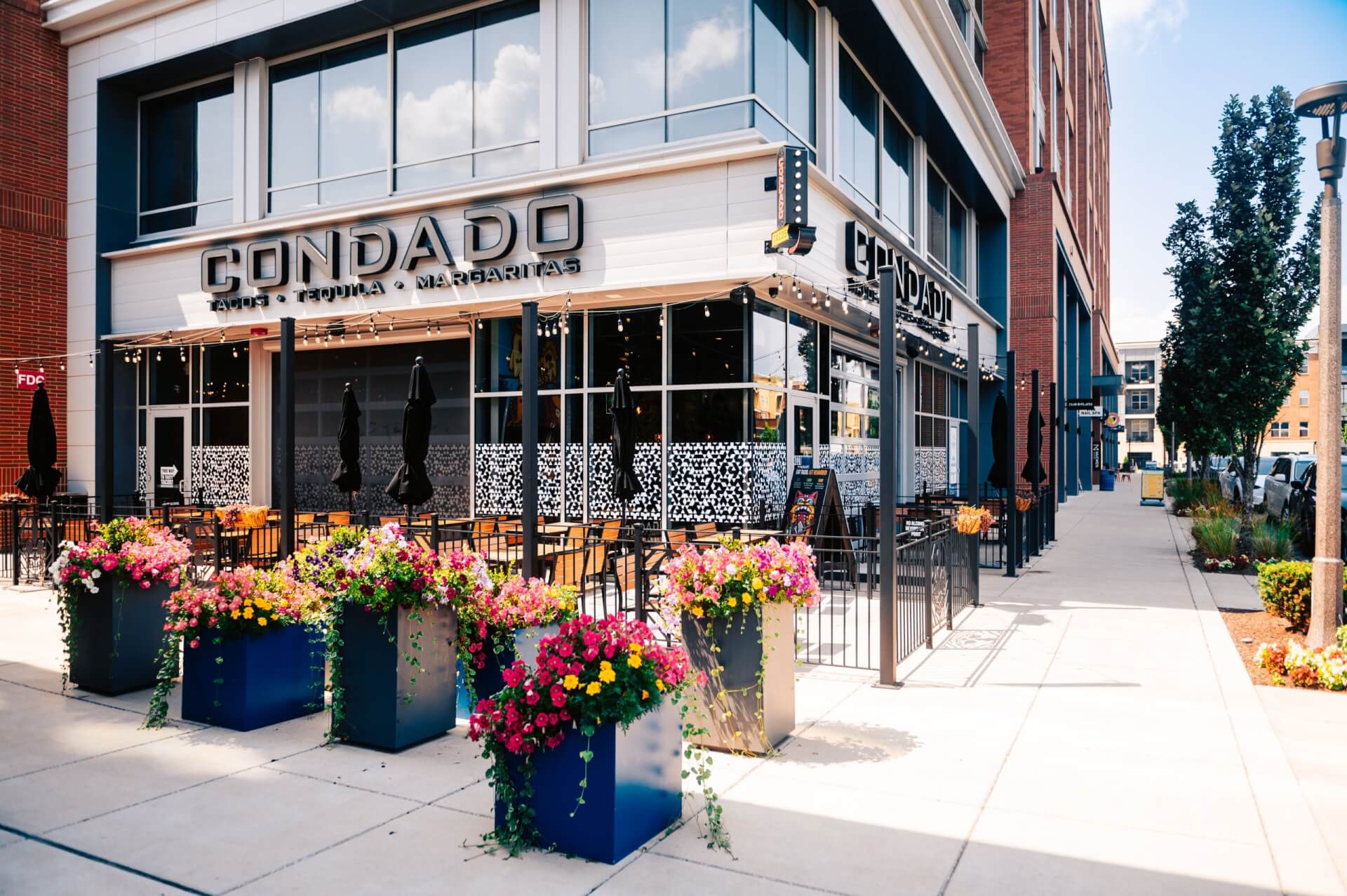 Group Services The exterior of a Condado Tacos restaurant with outdoor seating and colorful flower planters in Williamson County, Tennessee.