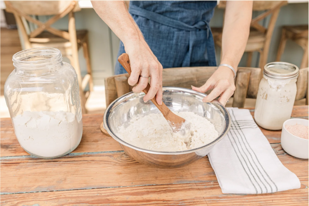 A person in a blue apron mixes flour in a metal bowl with a spoon in Williamson County, Tennessee.