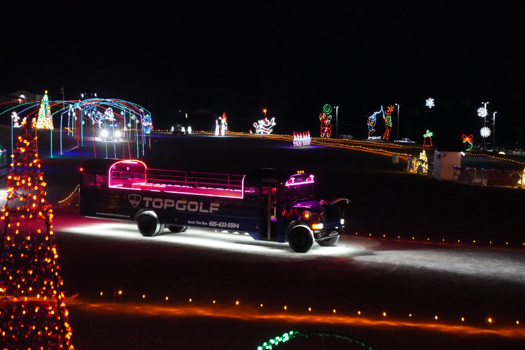 A Topgolf bus driving through a park decorated with Christmas lights at night in Williamson County, Tennessee.