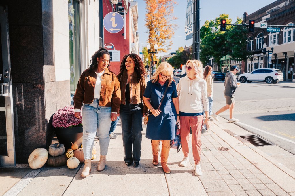 Four women walking together on a sunny city sidewalk during autumn in Williamson County, Tennessee.