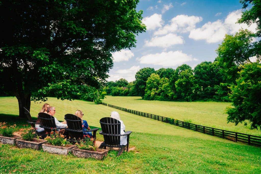 Three people sit in Adirondack chairs overlooking a lush green field with a fence in Williamson County, Tennessee.