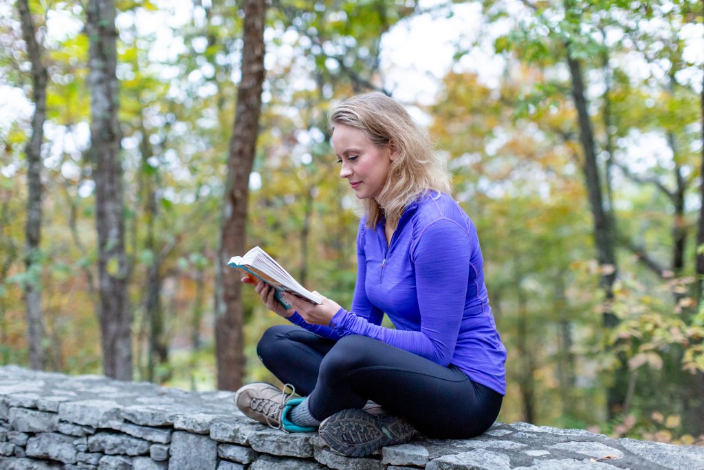 A woman in a purple shirt sits on a stone wall reading a book in Williamson County, Tennessee.