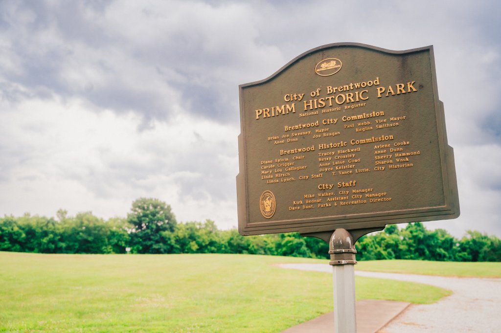 A historical marker sign for Primm Historic Park stands in a grassy field in Williamson County, Tennessee.