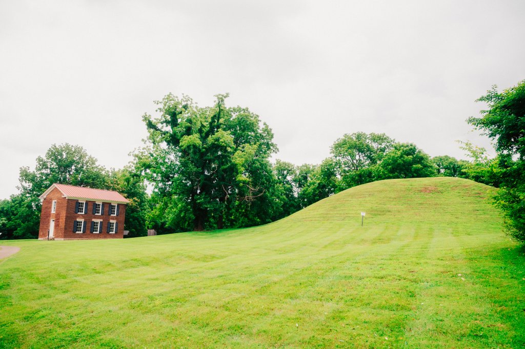 A brick house sits beside a large grassy hill under a cloudy sky in Williamson County, Tennessee.