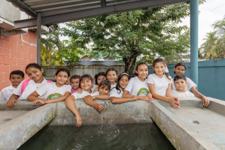Students from Honduras stand around a concrete water basin, leaning over the edge and looking toward the camera with smiling faces. 