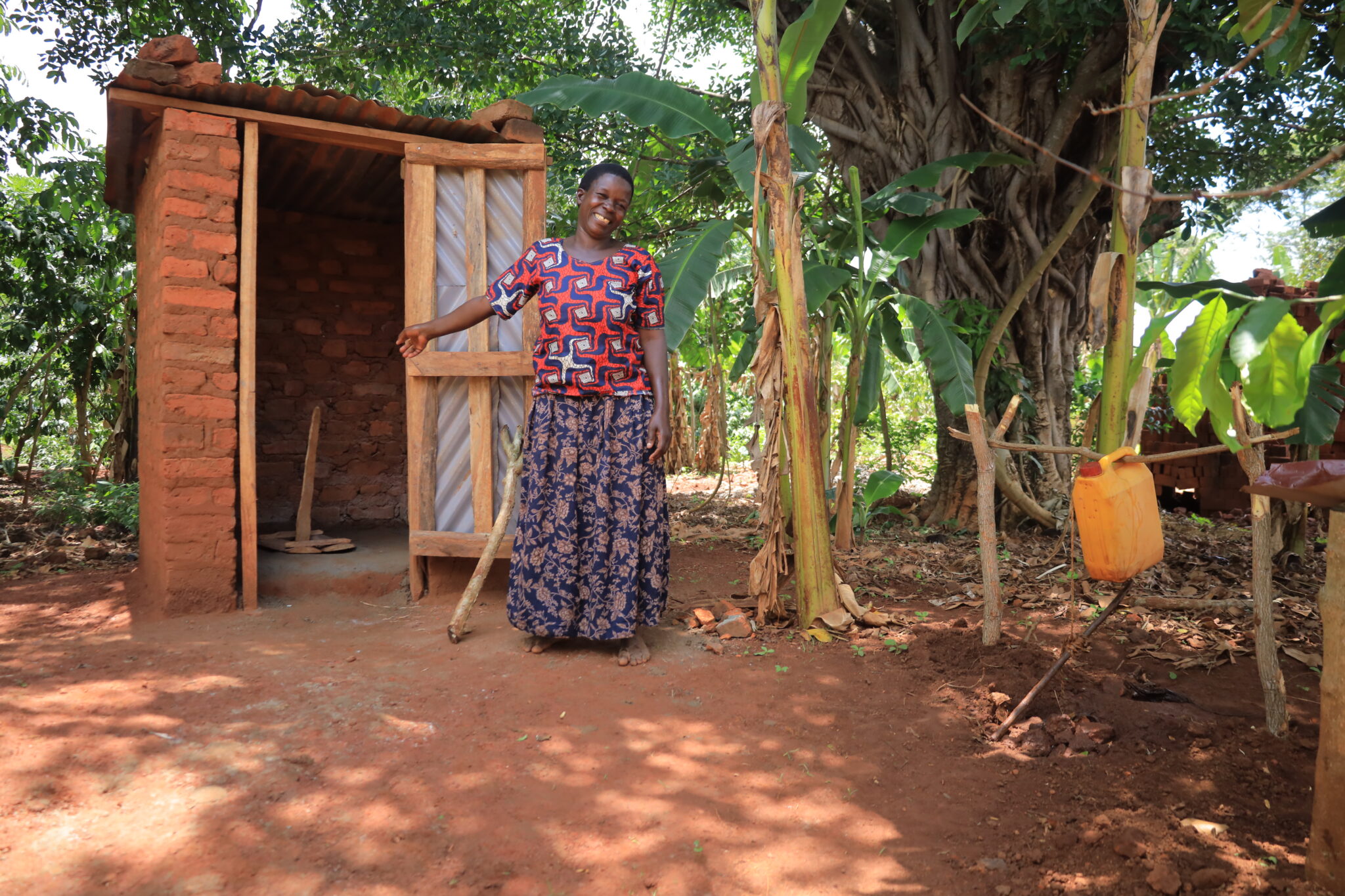 A woman stands in front of her newly constructed pit latrine and handwashing station.