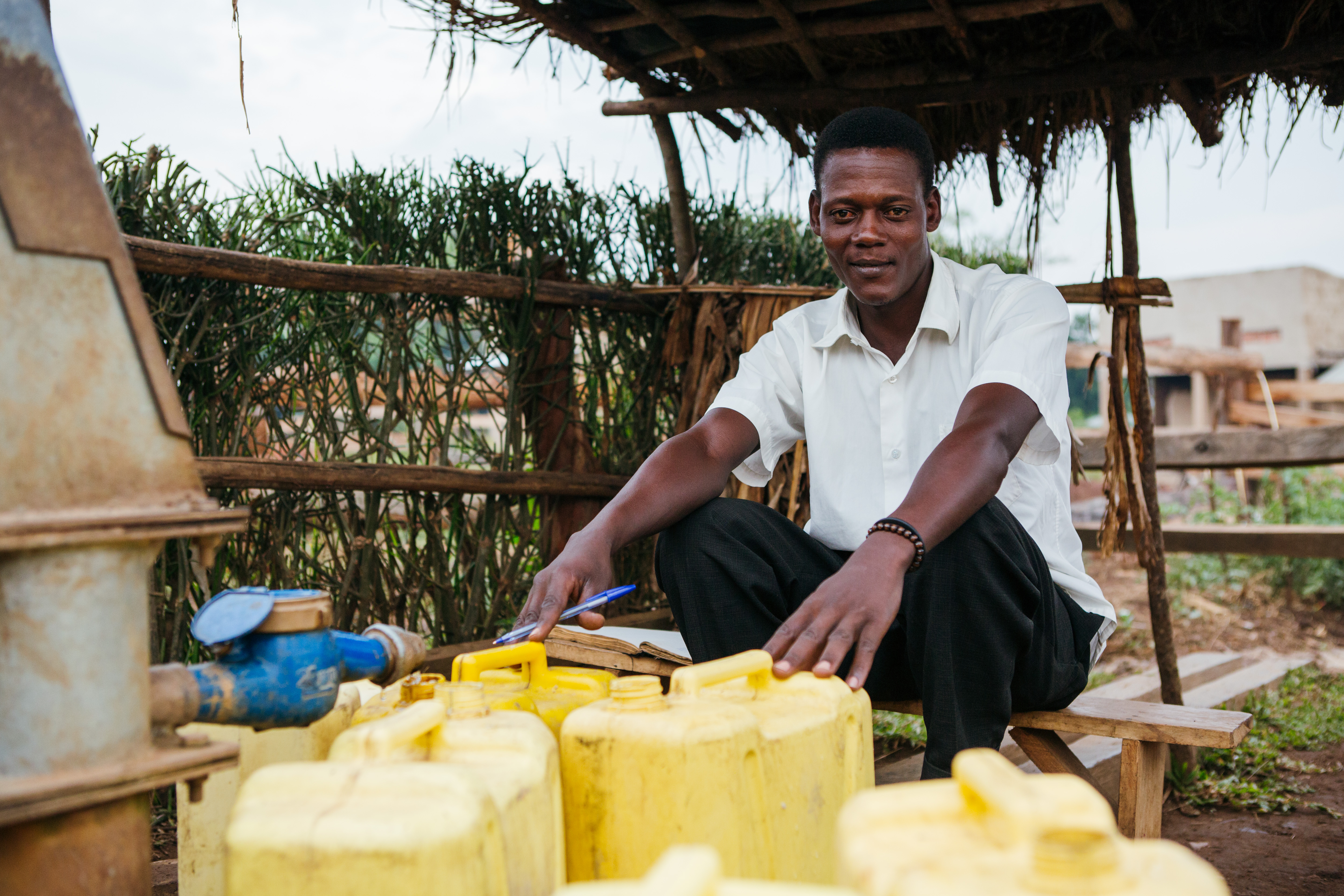 Laban, a water seller, sits next to the water point surrounded by yellow jerry cans